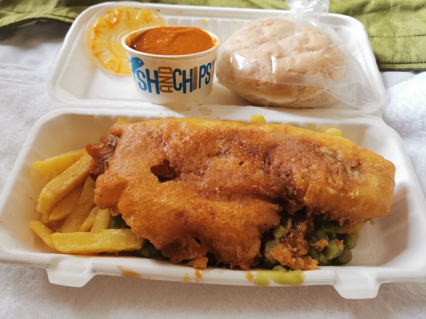 Battered fish and chips in a box with a sauce pot