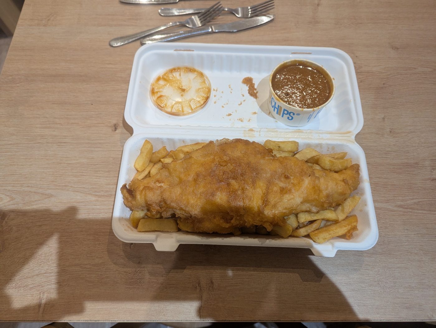 Fish and chips in a takeaway box with two sauce pots